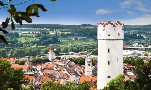 Der weiße Mehlsack Ravensburg ragt über die roten Dächer der Stadt. Im Hintergrund grüne Hügel und blauer Himmel.
