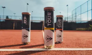 Tre tubi di palline da tennis Dunlop, tra cui un Dunlop Club All Court, su un campo in terra battuta.