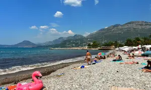 Słoneczny dzień na plaży w Barze, Czarnogóra. Ludzie opalają się, a w tle widać góry. Różowy flaming unosi się na wodzie.