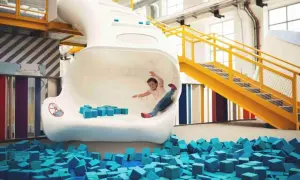 Kind rutscht in Techmania Pilsen durch eine weiße Röhre in einen Pool aus blauen Schaumstoffwürfeln.