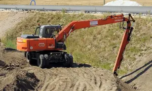 Pomarańczowa koparka Hitachi Zaxis 160W pracuje na budowie. Operator posiada odpowiednie uprawnienia na koparki, by sprawnie wykonywać prace ziemne.
