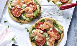 Zwei kleine Pizzen mit Pesto, Tomaten und Lachs auf einem Blech.