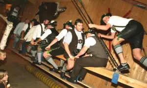 Männer in Lederhosen und Trachtenhemden auf einer Holzbank, bereit für ein Spiel auf der bayrischen Kirchweih.