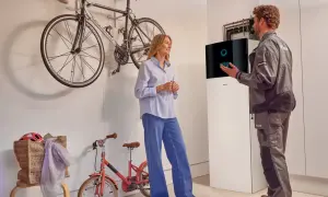 Técnico explica a una mujer el **rendimiento estacional aerotermia** junto a una unidad Daikin. Bicicletas colgadas al fondo.