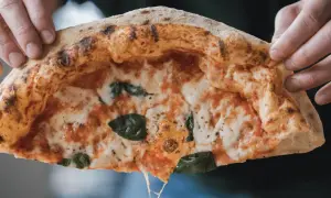 Hände halten ein Stück Pizza mit luftigem Rand, geschmolzenem Käse und Basilikum.