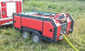 Nowa zabudowa pożarnicza na przyczepie, gotowa do akcji. Wąż strażacki zwinięty na bębnie, czekający na sygnał.