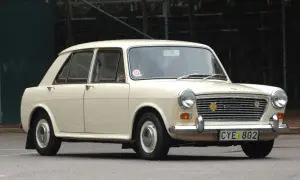 En krämvit Austin 1100 står parkerad på asfalt. Bilen har en klassisk design med kromade detaljer och en tydlig grill.