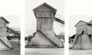 Strutture industriali in legno e cemento, tipiche delle opere di Hilla Becher, con scale esterne e nastri trasportatori.