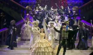 Upiór w operze: scena balu maskowego z tłumem w ekstrawaganckich strojach i maskach, sypiącym się konfetti.
