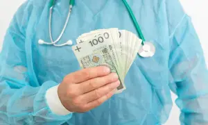Lekarz rezydent w niebieskim fartuchu trzyma w dłoni plik banknotów 100 zł. Pytanie brzmi: ile zarabia lekarz rezydent?