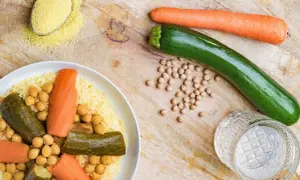 Un plat de couscous aux légumes, pois chiches, carottes et courgettes. Une cuillère de semoule est à côté.