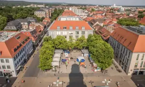 Marktplatz in Erlangen mit Ständen und Bäumen. Ein Schatten wirft sich über den Platz, vielleicht ein Geheimtipp für Fotografen.