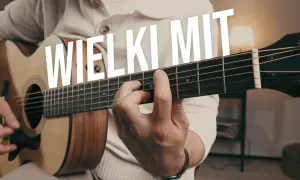 Ręka grająca na gitarze akustycznej, palce na gryfie. W tle biały napis "WIELKI MIT". Idealne ćwiczenia gitarowe.