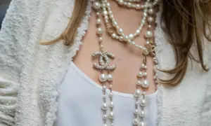 Eleganckie stylizacje z perłami: wielowarstwowy naszyjnik z logo Chanel i perłami na tle białej marynarki.
