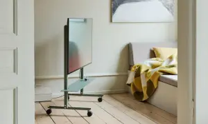 Moderner fernseher im schlafzimmer auf einem grünen Rollwagen, daneben eine gemütliche Bank mit karierter Decke.