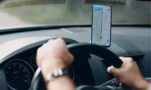 Ręce na kierownicy, smartfon z nawigacją na Androida pokazuje trasę.