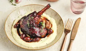 Une souris d'agneau braisée, nappée d'une sauce foncée, servie sur une purée onctueuse avec des olives et de l'ail rôti.