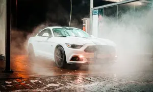 Biały Mustang w obłokach pary podczas mycia aut. Woda spływa po karoserii, tworząc efektowną mgiełkę.