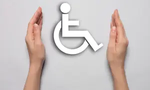 Dwie dłonie otaczają symbol osoby na wózku inwalidzkim, symbolizując wsparcie dla osób, na jakie choroby można dostać orzeczenie o niepełnosprawności.
