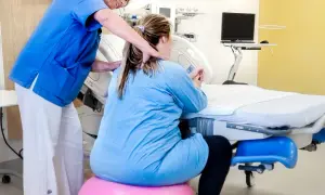 Barnmorska stöttar en kvinna i gravid vecka 36 som sitter på en rosa boll vid en förlossningssäng.