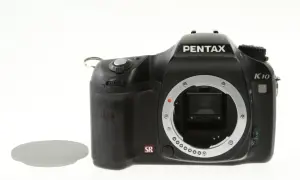 Czarny aparat Pentax K10 bez obiektywu, widoczna jego cmos matryca. Obok leży osłona.