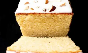 A slice of almond cake with white icing and chopped almonds on top, against a black background.