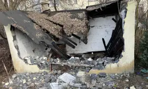 Zniszczony budynek po rozbiórce. Dach się zawalił, a ściany są wybite. Wokół leżą gruzy i drewniane belki.