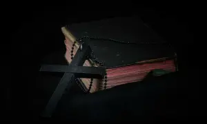 Czarny krzyż i paciorki różańca na starej księdze. Symbol wiary i modlitwa o spokój ducha w mroku.