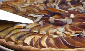 Une tranche de tarte aux nectarines, garnie d'amandes effilées, est coupée par un couteau.