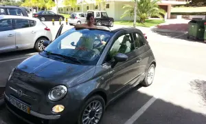 Frau lehnt sich aus einem grauen Fiat 500 Cabrio, bereit für eine Spritztour. Gute mietwagen portugal tipps für den Urlaub!