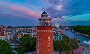 Widok na latarnię morską, diabelski młyn i port w Kołobrzegu o zachodzie słońca.