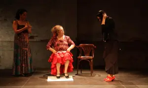 Tres mujeres en escena. Una sentada, con falda roja y blusa estampada, como **la Chana**. Otra de pie, con vestido largo y estampado. La tercera, de negro, con el pelo recogido.