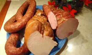 Wędzona szynka i kiełbasa na niebieskim talerzu, ozdobione gałązką choinki.