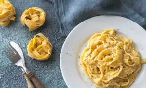 Un piatto di fettuccine alfredo cremoso, con nidi di pasta cruda e posate sul lato.