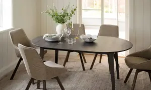 Ett runt mörkt matbord med fyra stoppade stolar runt sig. En vas med blommor, ljusstakar och en skål med frukt på bordet. En tidlös design klassiker.