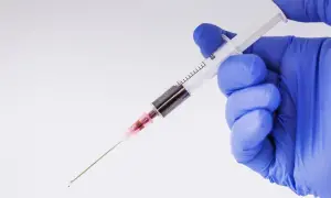Ręka w niebieskiej rękawiczce trzyma strzykawkę z ciemnym płynem. Jak leczyć hemofobię? Terapia może obejmować psychoterapię.