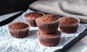Fem choklad cupcakes på ett bakplåtspapper. Två staplade på varandra i förgrunden, med tre till utspridda runt dem.