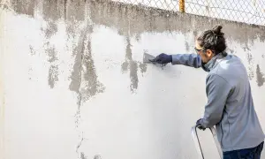 Hombre raspa pared desconchada, preparándola para pintura alquitranada.