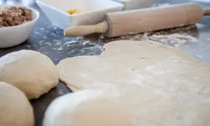 Pizzateig, Nudelhölzer und Schüsseln mit Zutaten auf einer Arbeitsfläche.