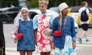Trzy dziewczyny prezentują modny styl ubioru młodzieży: sukienki w kwiaty, dżinsowe kamizelki i kolorowe torebki.