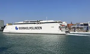 Biały prom "Bornholmslinjen Express" wypływa z portu, gotowy na podróż do Szwecji. W tle widać zabudowania portowe.
