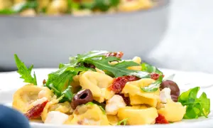 Ein köstlicher italienischer Salat mit Tortellini, Rucola, Oliven und getrockneten Tomaten auf einem Teller.