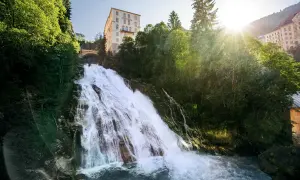 Tosender Wasserfall stürzt durch grüne Hänge in Bad Gastein Altstadt, wo sich ein imposantes Hotel über dem Naturschauspiel erhebt.