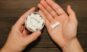 Dłonie trzymające pojemnik z białymi woreczkami nikotynowymi i jeden woreczek w dłoni. Czy snus jest legalny w Polsce?