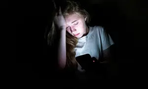 En tonåring med handen mot pannan, upplyst av en mobilskärm. Känslan av depression hos barn kan testas genom att observera sådana här stunder.