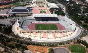 Widok z lotu ptaka na stadion olimpijski Montjuïc z zieloną murawą i trybunami. W pobliżu inne obiekty sportowe i tereny zielone.