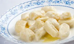 Pyszne kopytka z serem, polane śmietaną i masłem, na talerzu z niebieskim wzorem.