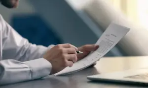 Mężczyzna w białej koszuli analizuje dokument, sprawdzając warunki, kiedy pracodawca nie musi wypłacić odprawy.