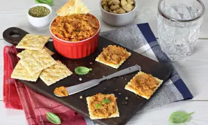 Pasta z suszonych pomidorów na krakersach, podana na desce z dodatkami.