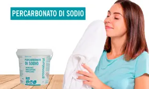 Donna annusa un candido asciugamano, felice del profumo fresco. Accanto, un barattolo di Percarbonato di Sodio, smacchiatore naturale per lavatrice.